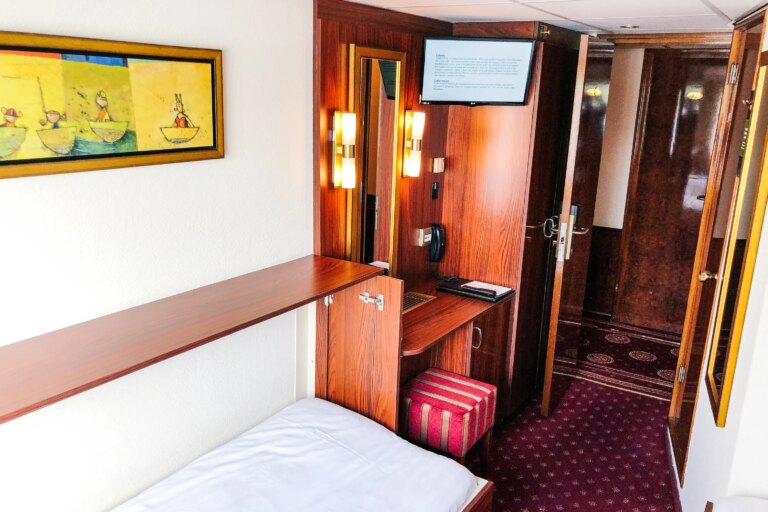 Interior of single cabin with bed, mirror and TV on a European river cruise ship.